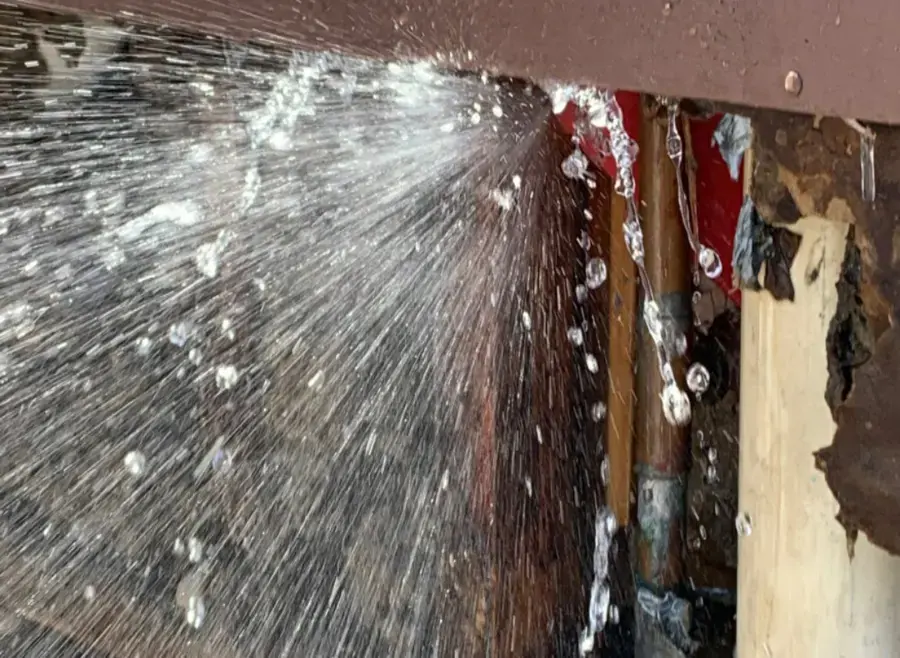 Water spraying from a burst pipe inside an opened wall