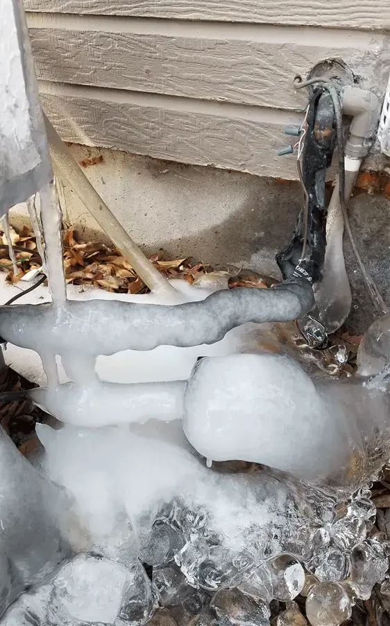 Ice built up around a frozen outdoor pipe along the siding of a house